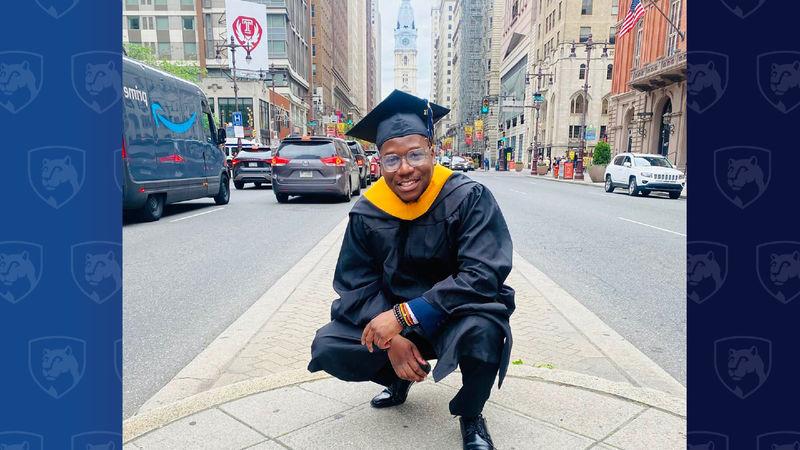 Man in cap and gown crouching near City Hall in Philadelphia